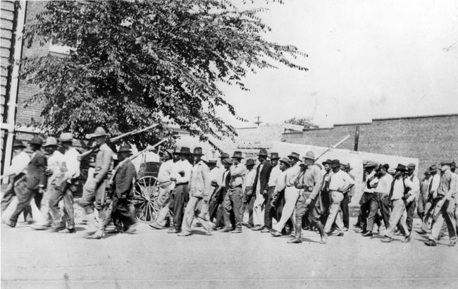 तुलसा रेस नरसंहार, तुलसा, ओक्लाहोमा, जून 1921 के बाद नेशनल गार्ड सैनिकों का एक समूह, संलग्न संगीनों के साथ राइफलें लेकर, निहत्थे अश्वेत पुरुषों को एक निरोध केंद्र में ले जाता है।