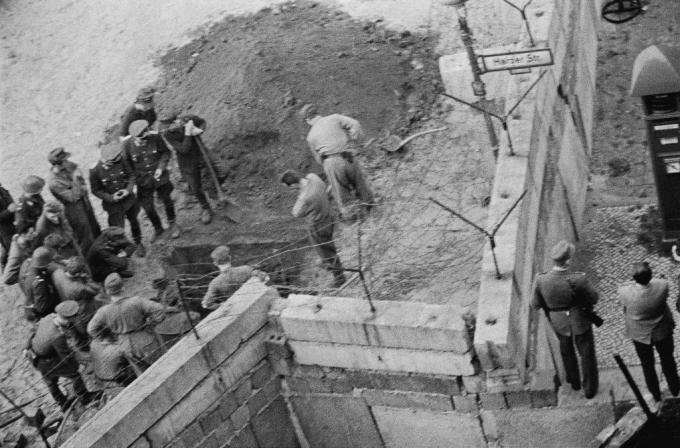 पूर्वी जर्मन सैनिकों का समूह बर्लिन की दीवार के नीचे खोदी गई एक सुरंग की जाँच करता है।