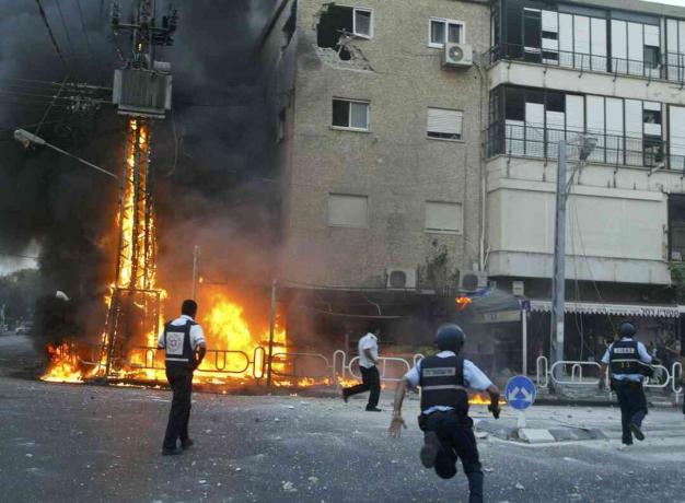 इजरायल के पुलिसकर्मियों ने 13 जुलाई, 2006 को इजरायल के उत्तरी शहर नाहर्या में हिजबुल्ला रॉकेटों के एक वॉली के बाद जलते हुए बिजली के तोरण और क्षतिग्रस्त इमारत के क्षणों के दृश्य को देखा।
