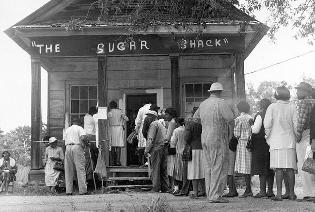 अफ्रीकी अमेरिकी मतदाता, ग्रामीण विलकॉक्स काउंटी, अलबामा में पहली बार मतदान करने में सक्षम हैं, 1965 में संघीय मतदान अधिकार कानून के पारित होने के बाद एक मतदान केंद्र के सामने लाइन में खड़े हैं।