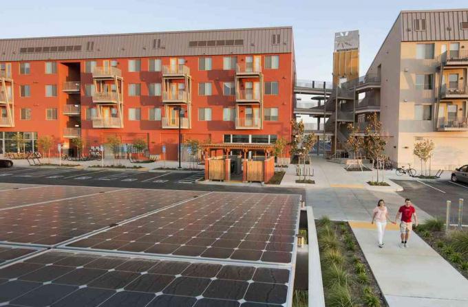 एक शून्य शुद्ध ऊर्जा समुदाय में, हरे रंग की इमारतों और सौर पैनलों के पास चलने वाले दो व्यक्ति