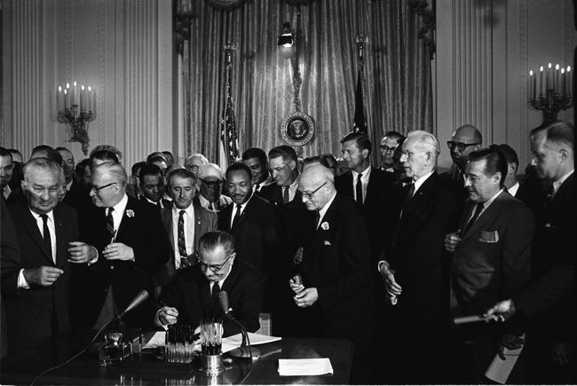 राष्ट्रपति लिंडन बी। जॉनसन 1964 के नागरिक अधिकार अधिनियम पर हस्ताक्षर करते हैं क्योंकि मार्टिन लूथर किंग, जूनियर, और अन्य, देखते हैं।